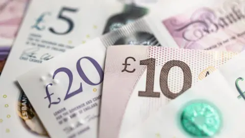 Close-up on several sterling cash notes, with a £5 note on the left, a £20 note in the middle and a £10 note on the right