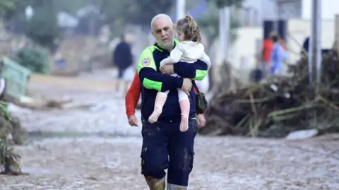 Getty Images A young girl is rescued by an emergency worker in a mud-covered street 