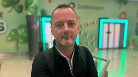 Mark O'Kane has short dark hair and a black jacket and shirt.