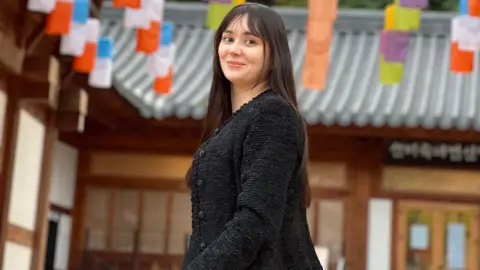 Mary Jeda Mary Jeda, dressed in black, smiles in a photo taken in Seoul. A wooden building with a tin roof can be seen behind her