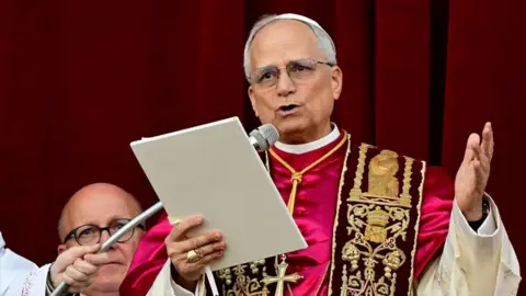 Pope Leo holds a piece of paper as he speaks from a balcony in Vatican City.