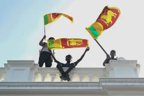 Drie jonge mannen zwaaien naar de fans van Sri Lanka vanaf de top van een witte betonnen balustrade