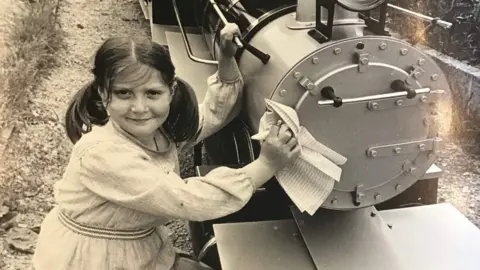 Emma Cole as a little girl in a black and white photo which shows her next to the miniature train.