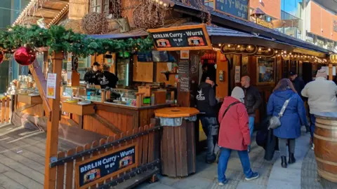 A bratwurst stall advertising German curry sausages with people walking past