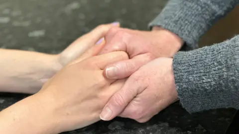 A close-up of two people's hands holding on to each other, there is black a kitchen top below.