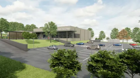 A light grey building with white lettering partially spelling out the words leisure centre. The building is surrounded by car park with some cars in white-lined parking spaces. The site is surrounded by trees growing from grass verges. 