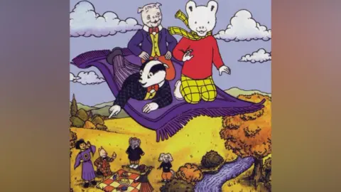 PA Media A cartoon drawing of a white bear, dressed in a red jumper and checked yellow scarf and trousers. He is on a purple flying carpet with a badger, dressed in a checked black suit, yellow shirt and red bow tie. There is also a pig, dressed in a blue suit, yellow shirt and red bow tie and trousers. Beneath them are andromorphic animals and a girl waving at them.