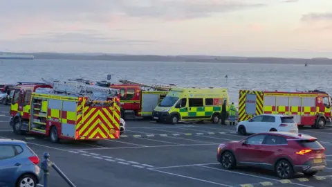Rich Patterson Fire engines and ambulances in a car park on the shore.