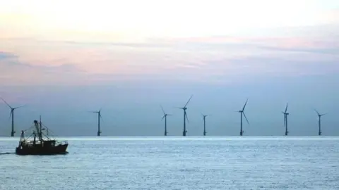 PA Media An offshore windfarm on the sea during sunset, with a fishing trawler in the foreground.