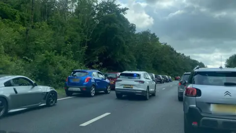 An unmarked police car with its blue lights on drives along the A38 in Devon to the scene of a crash. Both lanes of traffic have moved over to allow space for the vehicle to move through.