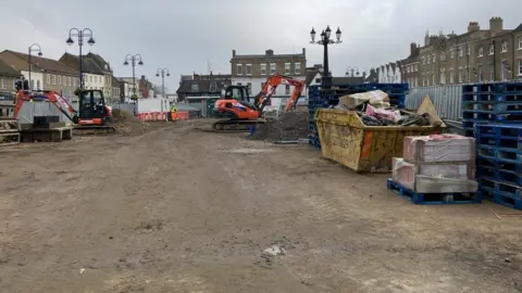 Seb Noble/BBC St Neots Market Square being razed by diggers, with all the paving taken up and skips full of waste
