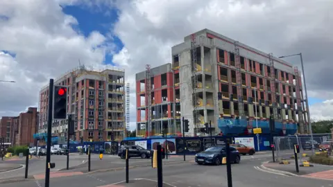 Photograph of the Hatters Yard development which is under construction in Stockport. The image shows a concrete frame, with traffic in the foreground.