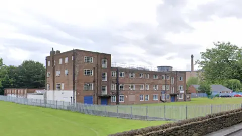 A three-storey brick building with multiple windows stands next to a sports field.