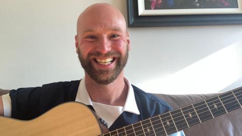 Nick Morgan smiling with his guitar and wearing his Scotland strip
