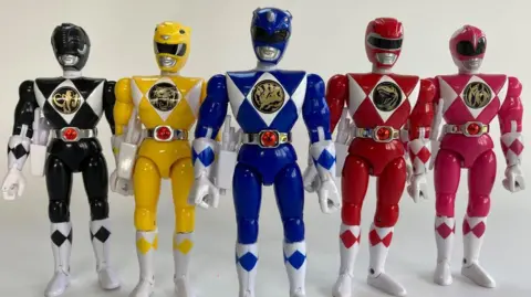 Matt Fox A group of Power Rangers action figures stood in a line, in the colours black, yellow, blue, red and pink.