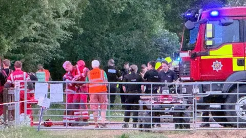 Phil Lack A group of emergency services personnel in a field. There is estimated to be about 12 people in the picture. To the right is a fire engine.