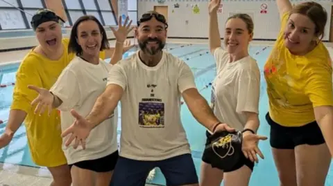 Swimmers outside the pool in yellow t-shirts and white t-shirts - hold their hands out in celebration