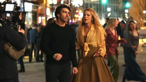 Getty Images Justin Baldoni and Blake Lively on the set of It Ends With US. They are mid-conversation. Baldoni is wearing all black. Lively has a brown dress on with an orange shirt over the top.