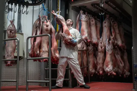 Getty Images Market worker wearing white protective clothing hanging prepared pork on hooks