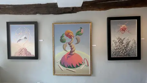 A wall with three surrealist paintings underneath a beam