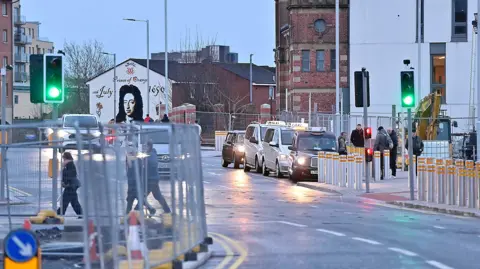 Pacemaker The road reopened - taxis are pictured lined up parked at the side of the road. There are people pictured on the pavement behind some traffic lights. On the left of the photo, there are construction fences.