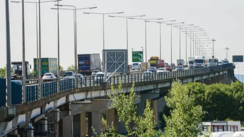 Tees flyover - both carriageways are visible and have a lot of vehicles driving over them. There are some green treetops visible at the bottom right, and the sky is a dull grey