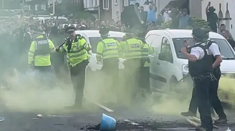 PA A large group of people confront police in a road in Southport