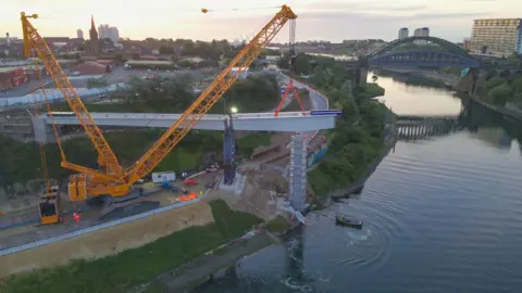 VolkerStevin A yellow crane holding up a section of the steel frame. The river is to the right of the photo.