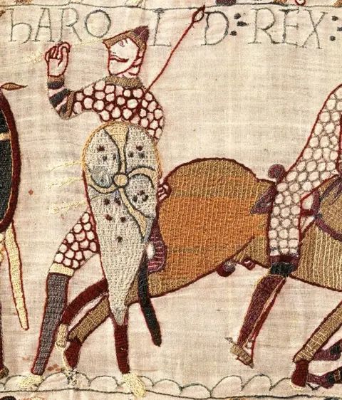Bayeux Museum A close crop shows Harold depicted as being shot with an arrow next to a horse, with writing reading 'Harold rex' with fabric detail.