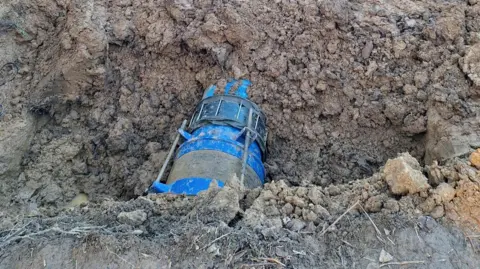 Southern Water A section of large, blue pipe, partially exposed but predominantly buried under dirt.
