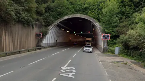 A picture of a large tunnel. There is a car and lorry traveling in it.