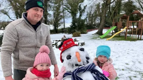 A man with two young girls, beside a snowman