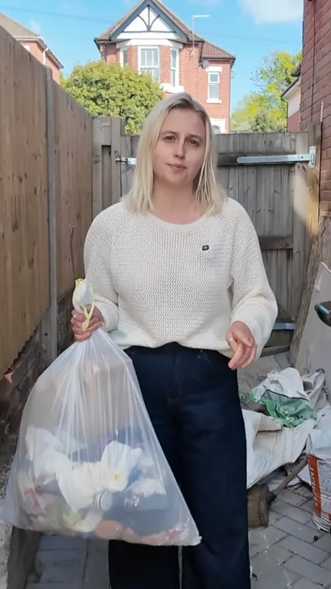 A woman with blonde hair holding a bin bag 