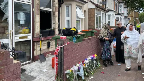 PA Media Flowers left outside the house as members of the community stand outside