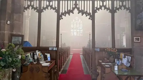 Shropshire Fire and Rescue Service The inside of a church with a long red carpet running between the pews and smoke hanging around the back of the church