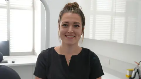 Shaun Whitmore/BBC Georgina Rowe, the practice manager at Friends Dental Practice in Norwich. She is looking at the camera and is smiling. Her hair is tied up and she is wearing a black outfit.