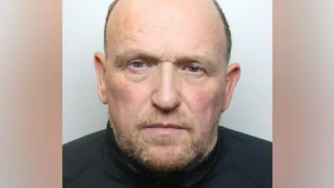 Martin has a brown greying beard, and cropped brown greyign hair and is wearing a black shirt.