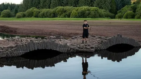 Stone bridge at the Llwyn-Onn Reservoir in Merthyr Tydfil in 2026. The bridge is visible above the water. A boy is standing on it