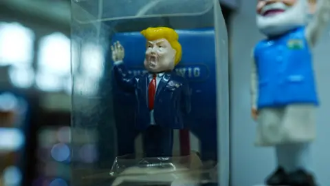 Xiqing Wang, Xiqing Wang A toy Trump in a blue jacket and red tie in a glass case in a stall in Yiwu.