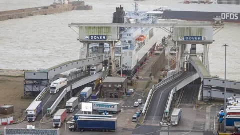 Getty Images A port terminal where numerous trucks and trailers are queued on ramps leading to a docked ferry. The weather is grey and overcast.