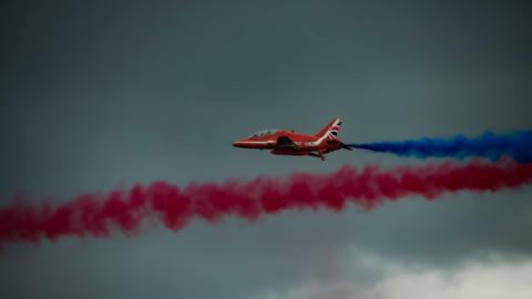 A red arrow in the sky, trailing blue smoke