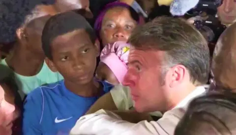 French President Emmanuel Macron in an animated conversation with a woman in a crowd in Mayotte