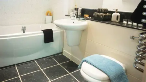 Getty Images A white bathroom with a bath, sink and toilet. The floor is made up of black tiles.