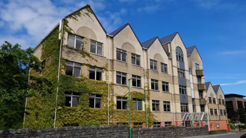 BBC States building, Sir Charles Frossard House, St Peter Port, Guernsey. A four storey building. It's a concrete colour and in this picture some of it is covered in plant life. 