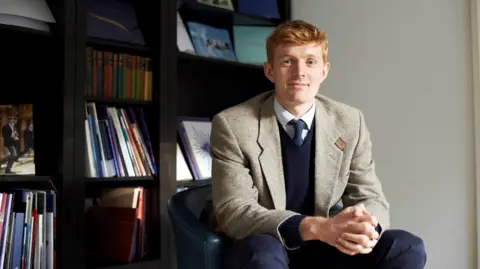 Will Orr-Ewing An image of Will Orr-Ewing sat in front of shelves filled with books