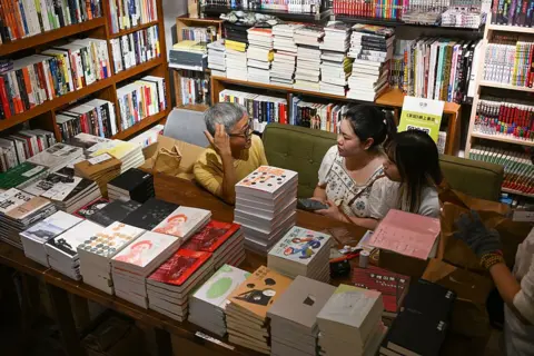 AFP via Getty Images Independent publisher Leslie Ng speaking to journalists at the Hunter Bookstore, surrounded by piles of books and packed shelves
