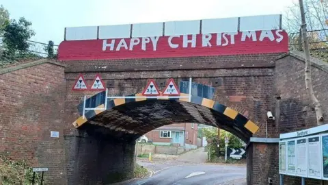 A bridge with red and white paint reading "Happy Christmas" across the top of the bridge.