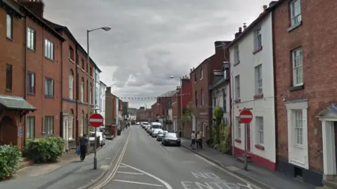 Google A street with rows of houses down both sides and bunting hanging over the street