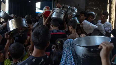 EPA Men carrying cooking utensils waiting in a crowded line for supplies