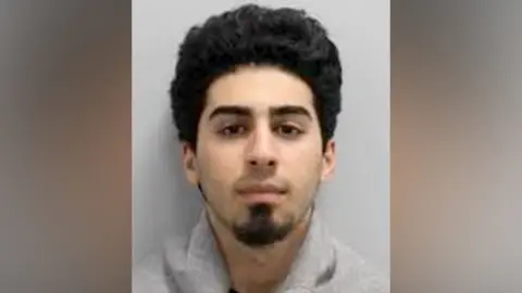 Police custody image of Marwan Khadir, a young man with curly black hair and a goatee beard.
